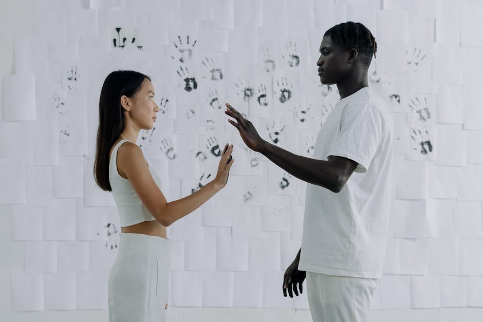A man and woman standing face to face in front of a wall covered with handprints, exploring themes of connection and diversity.